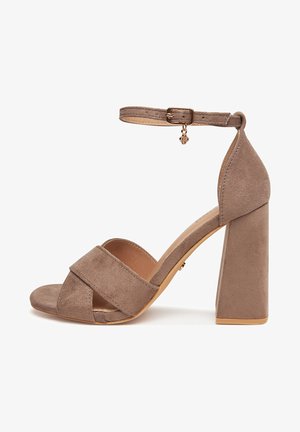 Sandalo da donna in camoscio marrone con tacco largo, cinturini incrociati sulle dita e cinturino regolabile alla caviglia con piccolo ciondolo.