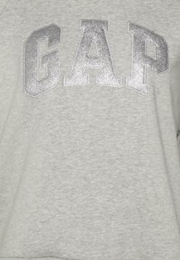 Felpa grigia con grandi lettere metalliche argento che spelling "GAP" sul davanti. Tessuto morbido con un design informale.