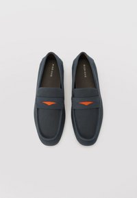 Marineblå perforerte loafers med en jevn overflate, oransje detalj, og en rund tådesign på en grå bakgrunn.