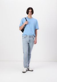 Világoskék pamut póló, slim fit világoskék farmernadrág és fekete keresztbody táska. A cipő fehér, sötétszürke és fekete akcentusokkal. Egyszerű design.