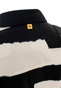 Relaxed-fit shirt with a black and cream abstract pattern, featuring a flat collar and a gold hardware tag on the back neck.