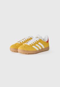 Geel suède sneakers met een witte drie-strepen ontwerp, witte veters en een gumrubberen zool. Voorzien van een rode accent op de hiel.