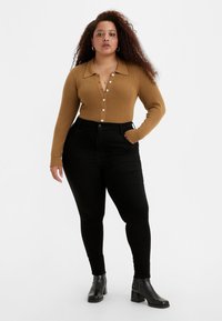 Top marrón de manga larga con textura acanalada y cierre de botones, combinado con jeans skinny negros de cintura alta. Botines negros con tacón cuadrado.