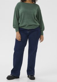 Groene, gestructureerde trui met een ronde halslijn en verlaagde schouders, gecombineerd met donkerblauwe, recht gesneden jeans en zwarte platform schoenen.