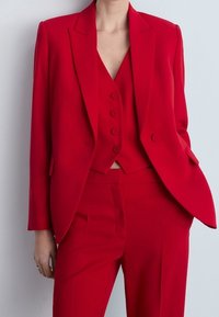 Costume rouge sur mesure avec un blazer cintré et un gilet doté d'un col cranté et d'une fermeture à bouton, associé à un pantalon à jambe droite.