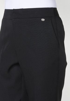 Pantalons noirs ajustés avec une texture lisse, des plis subtils et un petit logo métallique sur la taille.