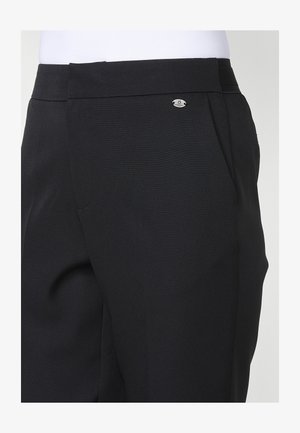 Pantalones negros de corte ajustado con una textura suave, pliegues sutiles y un pequeño detalle de logo metálico en la cinturilla.