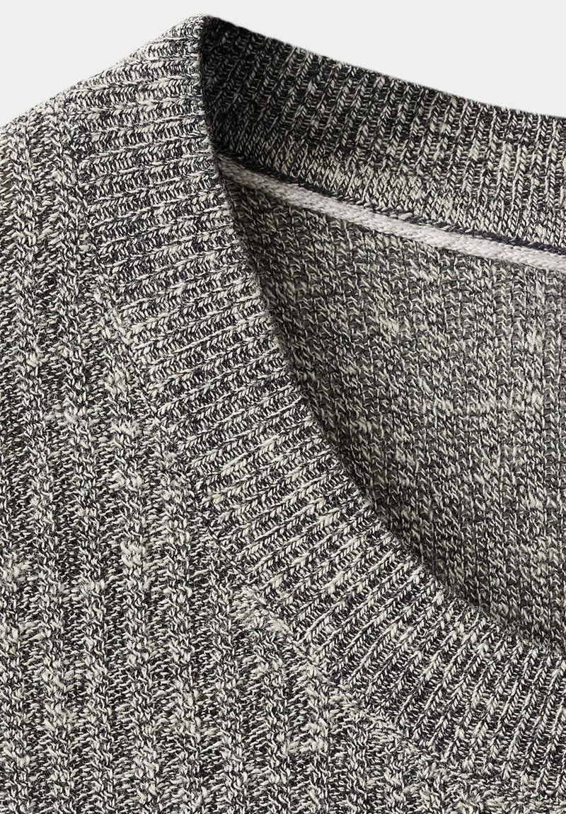 Gros plan sur l'encolure d'un pull tricoté gris et blanc avec un col côtelé et un motif torsadé texturé.