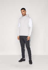 Grå pullover hoodie med hvide ærmer og design med tre striber, parret med sorte joggers med sidestriber og casual sorte sneakers.