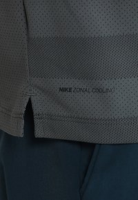 Maglietta Nike Zonal Cooling in grigio scuro, con trama in rete, strisce orizzontali e uno spacco laterale. Logo stampato vicino all'orlo.