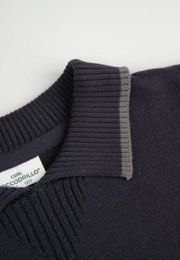 Kołnierz granatowego, dzianinowego swetra o prążkowanej fakturze, z kontrastującym szarym paskiem na krawędzi. Widoczna metka z marką i rozmiarem.