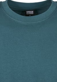 Teal színű, rövid ujjú pamut póló, kerek nyakkivágással, a gallér belsejében "URBAN CLASSICS" felirattal.