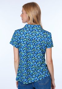 Short-sleeve shirt in blue with a floral print, featuring green leaves and a collar. The back has pleats for style and comfort.