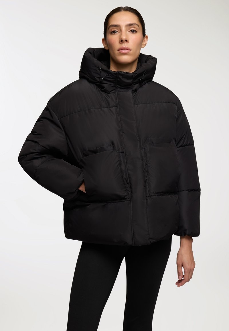 Czarna kurtka puchowa z kapturem, o pudełkowym kształcie, pikowanym wzorze, z kieszeniami na łatki i elastycznymi mankietami, wykonana z gładkiego, błyszczącego materiału.