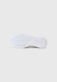Semelle blanche de chaussure de sport avec des motifs de grip texturés et un logo subtil près du talon, montrée par le dessous sur un fond uni.