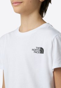 Tricou alb din bumbac, cu un logo negru pe partea stângă a pieptului. Design clasic cu guler rotund și mâneci scurte.