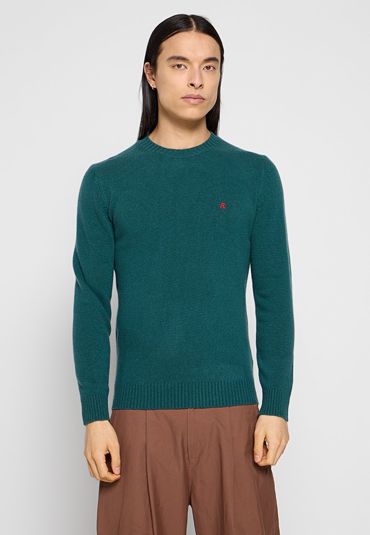 Teal trui met een ronde hals, lange mouwen, geribde manchetten en zoom, heeft een klein rood logo op de borst, zachte gebreide textuur.