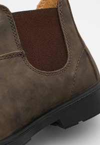 Bottine en cuir marron avec panneau latéral élastique, surface texturée, coutures marron contrastantes et semelle en caoutchouc.