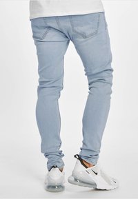 Vaaleansiniset skinny-farkut, joissa on sileä pinta, viisi taskua ja huomaamattomat ompelu yksityiskohdat. Yhdistetty valkoisiin ja mustiin urheilukengiin.
