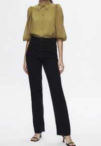 Blouse à carreaux vert olive avec des manches bouffantes, associée à un jean noir taille haute et des sandales à talons noirs.
