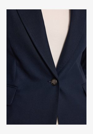 Granatowa marynarka z teksturowanej tkaniny, z pojedynczym dużym czarnym guzikiem, klapami w kształcie notch oraz bocznymi kieszeniami. Dopasowany krój z delikatnym połyskiem.