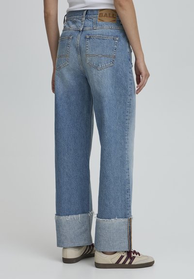 Lichtblauwe spijkerbroek met een wijde pijp, uitgerafelde zomen en een tan lederen label achteraan. Beschikt over twee achterzakken en een ontspannen pasvorm.