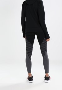 Czarna bluza z kapturem i czarne legginsy z szarymi paskami. Materiały wydają się elastyczne i miękkie. Obuwie jest czarne z białą podeszwą.