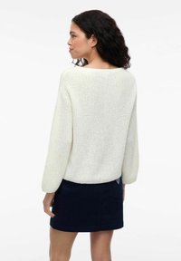 Biały dzianinowy sweter o luźnym kroju i długich rękawach, zestawiony z ciemnoniebieską spódnicą. Teksturowany materiał o swobodnym fasonie.