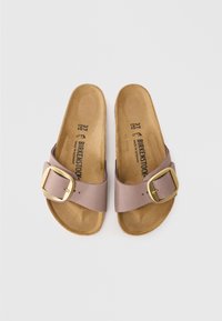 Ljuslila slide-sandaler med bred rem, guldspänne och en texturerad brun fotända. Storleken är angiven som 37/240.