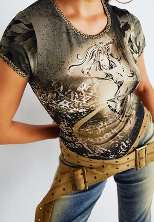 Vrouw die een aansluitend bedrukt T-shirt draagt met een gestileerde vrouwelijke figuur en abstracte patronen, gecombineerd met vervaagde spijkerbroek en een brede lichtbruine riem.