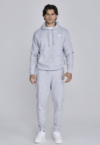 Light grey sweatshirt with a hood and front pocket, paired with matching sweatpants. Features ribbed cuffs and a logo on the chest.