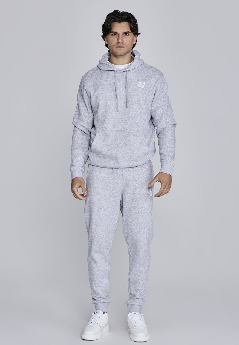 Light grey sweatshirt with a hood and front pocket, paired with matching sweatpants. Features ribbed cuffs and a logo on the chest.