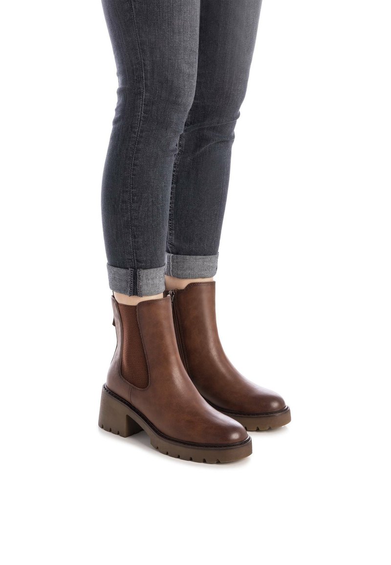 Stivaletti marroni in pelle con pannello laterale texture, punta arrotondata e tacco spesso. Indossati con jeans scuri risvoltati.