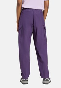 Purple, loose-fitting cargo pants with side pockets and an elastic waistband, paired with gray outdoor shoes. Smooth fabric texture.