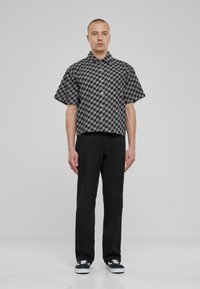Camisa de cuadros negra y gris de manga corta con botones, combinada con pantalones negros y zapatillas negras. Diseño simple con un corte recto.