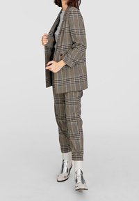 Kostkovaný blazer a kalhoty v béžové, hnědé a černé barvě, kombinované se šedým topem a stříbrnými nízkými botami. Hladká látka se strukturovaným střihem.