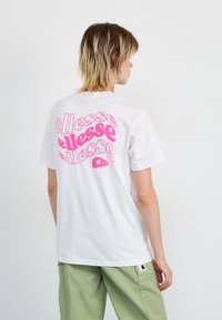 T-shirt en coton blanc avec un grand graphisme rose "ellesse" au dos. Manches courtes, coupe classique, texture lisse et design simple.