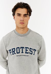 Grijze sweatshirts van een katoenmix, met een ronde hals en geribbelde manchetten. "PROTEST" logo in donkerblauw gedrukt op de borst.