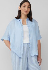 Lichtblauwe linnen oversized overhemd met korte mouwen, knopen aan de voorkant, gecombineerd met gestreepte lichtblauwe broek. Eenvoudig en casual ontwerp.