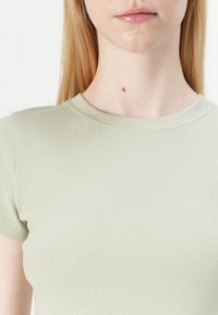 Light green fitted ribbed T-shirt with a round neckline and short sleeves. Fabric appears soft and stretchy. Minimalistic design with subtle texture.