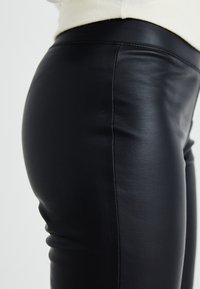 Black leather pants with a slim fit, featuring a smooth texture and a high waistband. Side stitching detail visible.