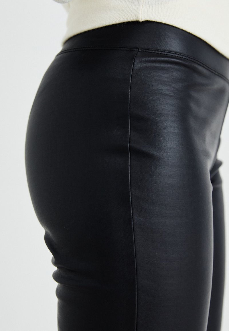 Pantaloni in pelle nera con vestibilità slim, caratterizzati da una texture liscia e una fascia alta in vita. Visibile il dettaglio delle cuciture laterali.