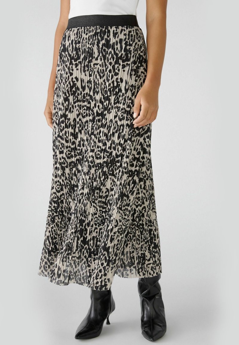 Femme portant une jupe midi plissée à imprimé léopard noir et blanc avec une ceinture noire et des bottines noires à bout pointu et talon.