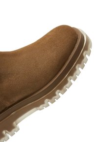 Bottine en suede marron avec une semelle en caoutchouc blanc épaisse, présentant un dessus texturé et un design à bout rond.