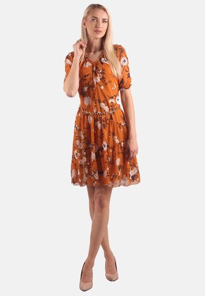 Oranges Blumenkleid mit kurzen Puffärmel, einem Taillengürtel und gestuften Rüschen. Der Stoff ist leicht und durchscheinend. Neutrale Absätze runden den Look ab.