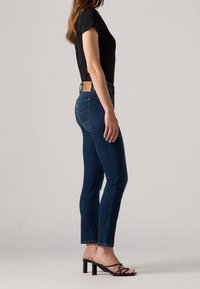 Jeans in denim blu scuro con una vestibilità slim e taglio alla caviglia, caratterizzati da una patch in pelle sulla vita posteriore e dettagli di cucitura sottili.