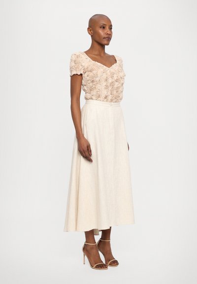 Beige blomstret topp med korte ermer, sammen med en lys kremfarget lang skjørt og nude høye hæler med stropper.