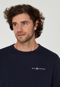 Camisa de manga larga navy hecha de tejido suave, con cuello redondo y un sutil logo blanco en el pecho.
