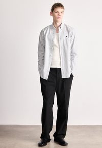 Λευκό και μπλε ριγέ πουκάμισο με κουμπιά πάνω από λευκό αμάνικο, συνδυασμένο με μαύρο παντελόνι και μαύρα παπούτσια· άνετη εφαρμογή, μακριά μανίκια, λογότυπο διακοσμητικό.