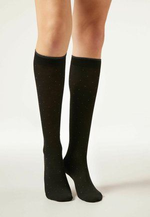 Chaussettes noires montantes en tissu lisse, présentant un motif à pois avec des accents bleus. Le haut est doté un bord côtelé pour plus de confort.